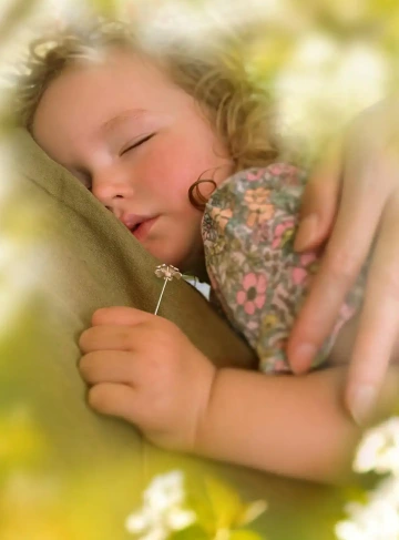 Holčička v náručí ženy drží stříbrnou květinu, dárek k narození holčičky