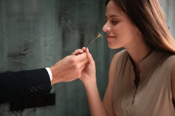 Krásná mladá žena vonící si ke zlaté květiny od muže, luxusní dárek k Vánocům pro ženu