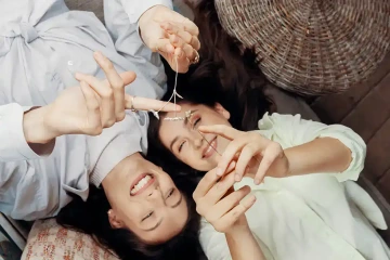 Sisters lying leading each other and laughing at flowers of silver, a gift for a sister from a rare garden