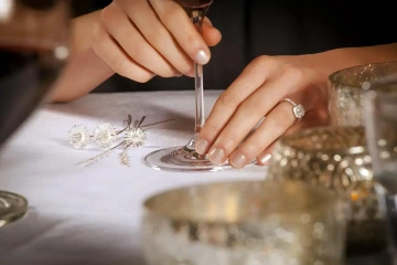 Woman's hands with a glass of wine and silver flowers placed on the table