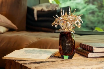 Bouquet of golden flowers in a Moser vase, on a table with books, luxury home decor