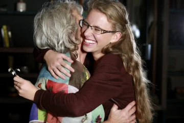 Mother hugging her daughter who’s holding a flower given to her as a graduation gift