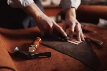 Ruce řemeslníka vyrábějící koženou luxusní tašku pro muže