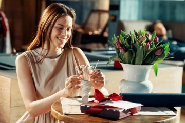 A smiling, beattiful woman with gifted jewelelry flowers and live flowers in a vase, unique birthday gift for a woman