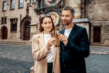A man and a woman in front of the Prague Astronomical Clock with unique Czech jeweller's flowers
